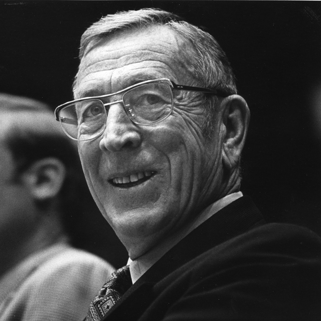 Coach Wooden in a suit, waiving.